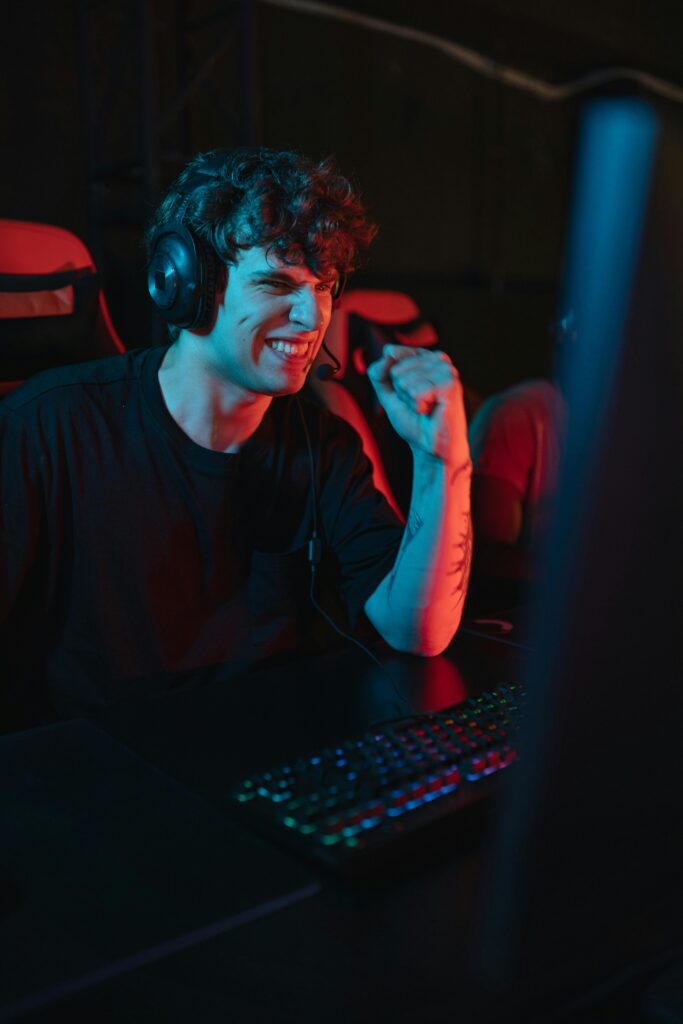 Caucasian man with headset showing excitement after gaming success in dimly lit room.