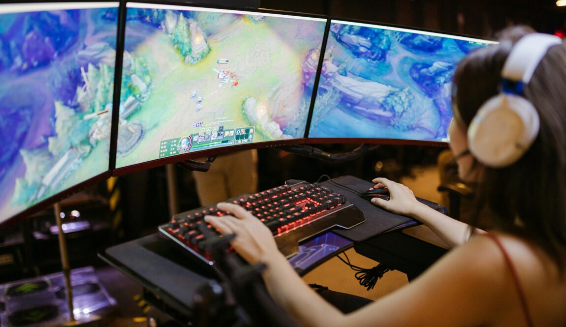 A young woman intently gaming on a multi-screen setup, showcasing vibrant gaming visuals.